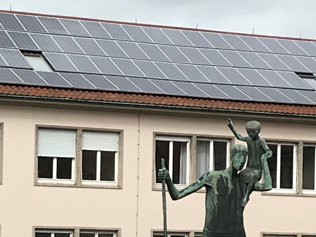 Christophorus-Skulptur vor einem kirchlichen Gebäude mit Photovoltaik auf dem Dach