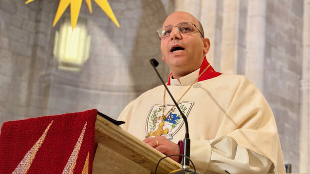 Geistlichen in weiß-rotem liturgischem Gewand, der in einer Kirche am Pult steht und spricht.